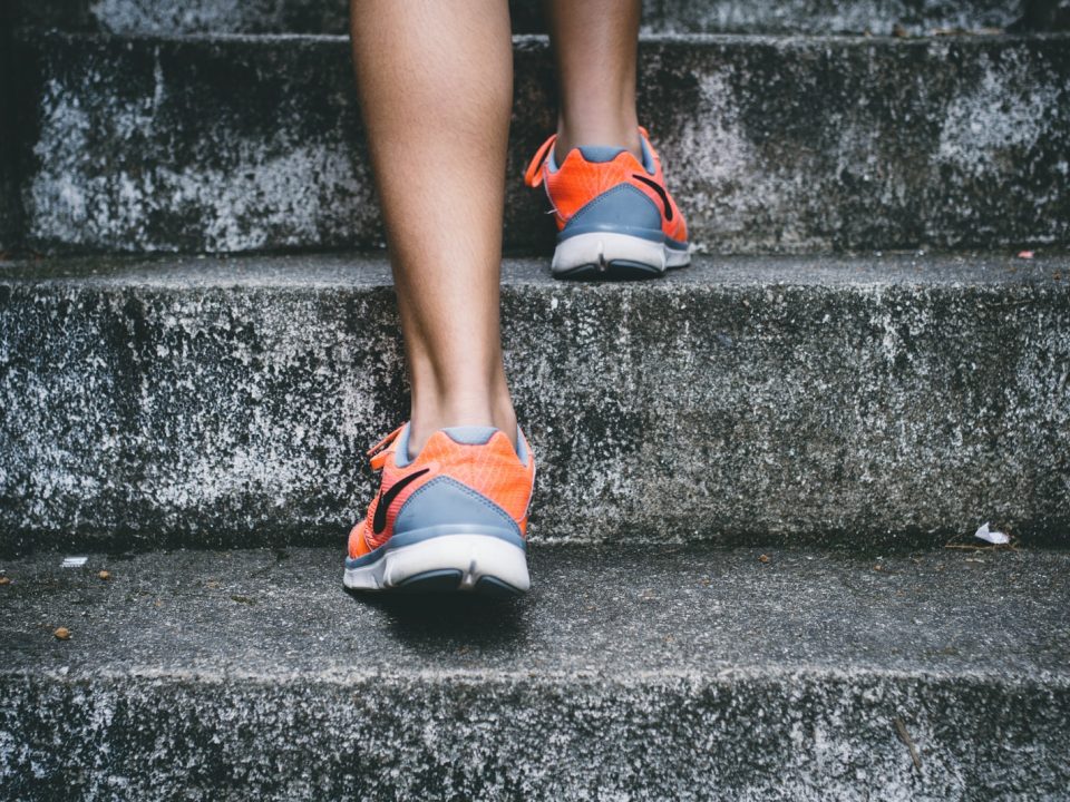person wearing orange and gray Nike shoes walking on gray concrete stairs